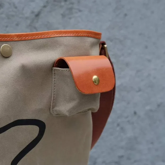 Dedicated external earbud pocket detail on the Leather Canvas Unisex Bucket Bag for easy tech access.