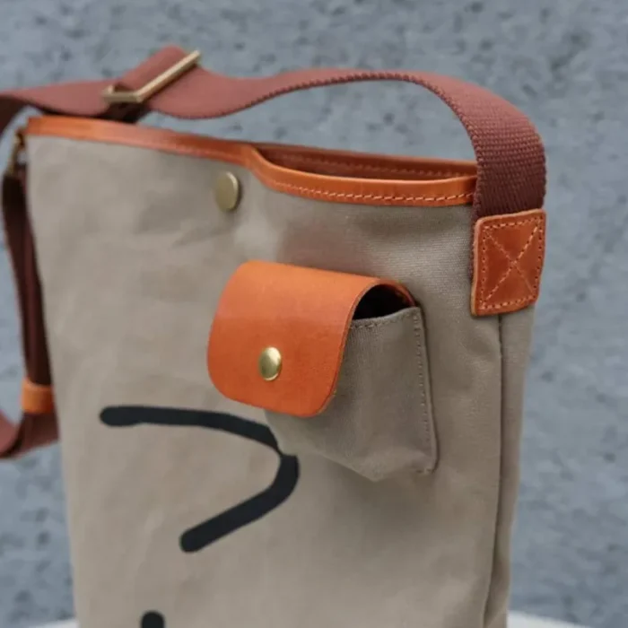 Dedicated external earbud pocket detail on the Leather Canvas Unisex Bucket Bag for easy tech access.